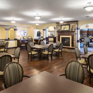 A spacious dining room with wooden floors, arranged tables and chairs, and a fireplace.