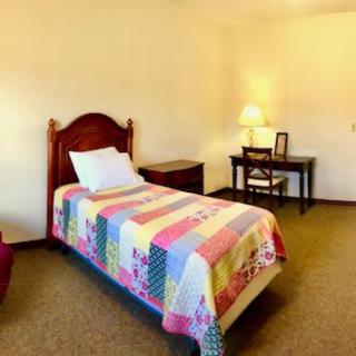 A cozy bedroom with a single bed adorned with a colorful quilt, alongside a small desk and lamp.