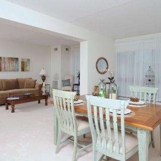 A cozy open-concept dining and living area with a wooden dining table, pastel chairs, and a comfortable sofa.