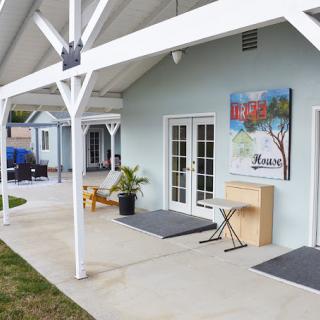 A patio area outside a light-colored building featuring artwork, potted plants, and outdoor furniture.
