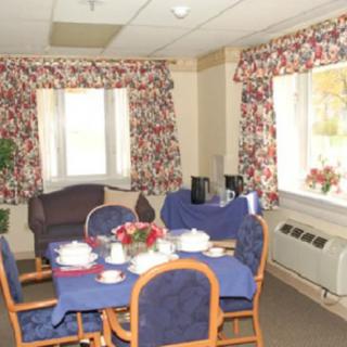 A cozy dining room with a table set for tea, featuring floral curtains and large windows.