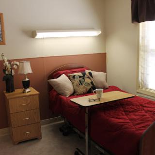 A cozy bedroom featuring a bed with red bedding, a nightstand with a lamp, and a small table tray.