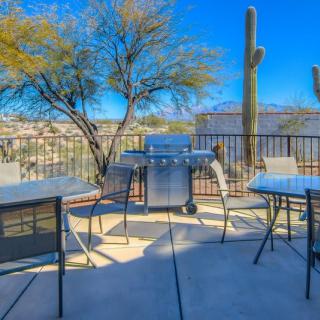 A sunny desert patio with a grill, tables, chairs, and cactus plants.