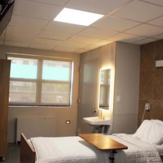A clean and modern hospital room with a single bed, window, and soft lighting.