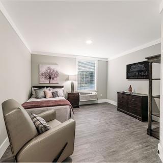 Modern and cozy bedroom with neutral tones, featuring a comfortable chair, wall-mounted television, and elegant wooden flooring.