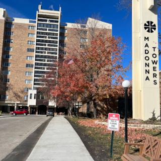 A residential building named Madonna Towers with autumn trees and a clear sky.