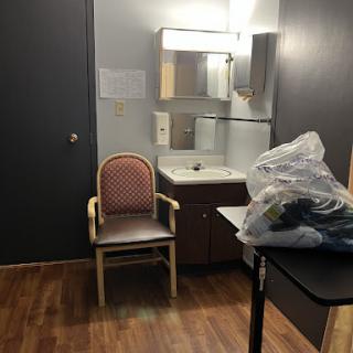 A simple interior of a room featuring a chair, mirror, and a table with some items.
