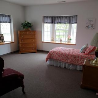 A cozy bedroom with a bed, dresser, and windows letting in natural light.