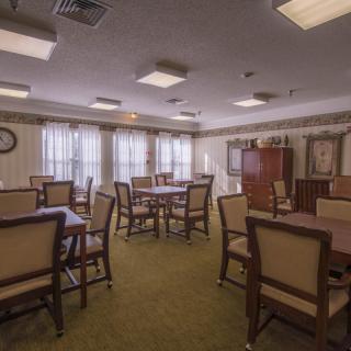A cozy dining room with multiple tables and chairs, well-lit by overhead lights and natural window light.
