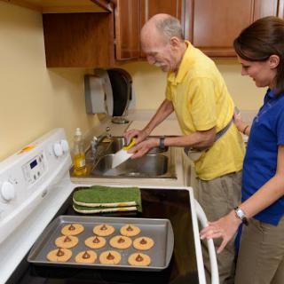 An elderly man and a caregiver working together in the kitchen, preparing cookies.