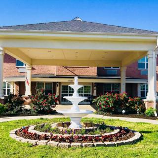 A beautifully landscaped entrance featuring a fountain in front of a brick building.