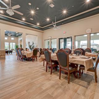 A spacious dining room with elegantly set tables and chairs, ceiling fans, and large windows providing natural light.