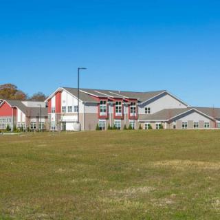 A modern residential building set against a clear blue sky with an open grassy field in the foreground.
