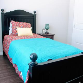 A cozy bedroom with a single bed featuring a turquoise blanket and decorative pillows.