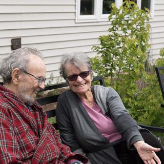 An elderly couple sitting together and smiling in a garden setting.