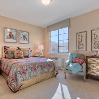 A well-decorated bedroom featuring a cozy bed, armchair, and large window allowing natural light to fill the space.