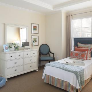 A neatly arranged bedroom with a single bed, dresser, and chair near a window.