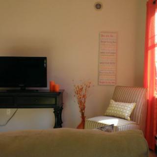 A cozy living room with a television, a cushioned chair, and bright curtains.