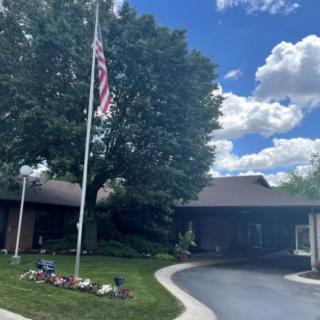 A residential house with a driveway and an American flag, surrounded by trees under a partly cloudy sky.