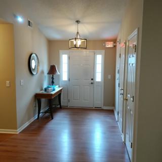 A cozy entryway with hardwood flooring, featuring a table with a lamp and mirror, illuminated by a chandelier.