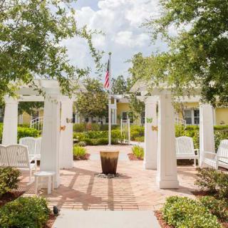 A beautiful garden featuring a pergola with benches, surrounded by lush greenery and centered around a flagpole.