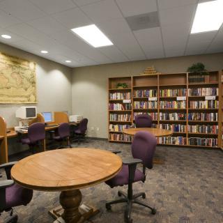 A cozy library space with bookshelves, tables, chairs, and computers for study and research.