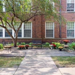 A serene garden area with benches, flowers, and trees in front of a brick building.