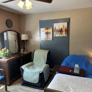 A cozy bedroom with a comfortable chair, a dresser with a mirror, and colorful artwork on the wall.