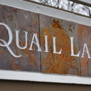 A rustic sign displaying the text 'QUAIL LANE'.