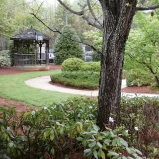 A serene garden featuring a winding pathway, surrounded by lush greenery and a gazebo.