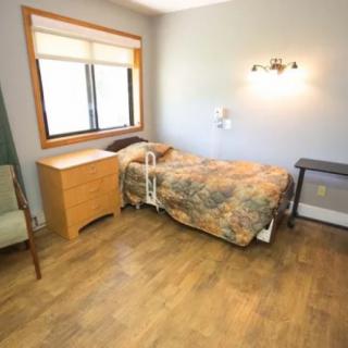 A simple bedroom with a hospital bed and wooden flooring.
