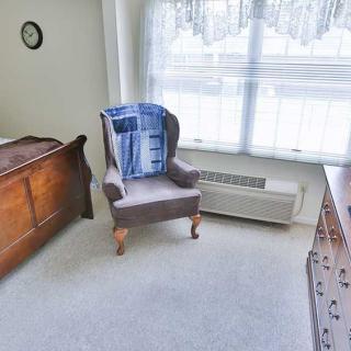 A cozy bedroom corner with a chair and dresser near a sunlit window.