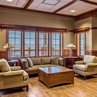 A cozy living room with comfortable sofas and armchairs, featuring wooden flooring and large windows.