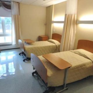 A hospital room with two beds, each equipped with wheeled over-bed tables and separated by curtains.