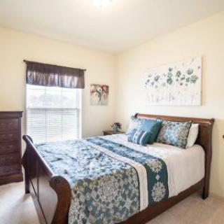 A cozy bedroom featuring a wooden bed with floral bedding and wall art, illuminated by natural light from the window.