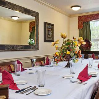 A dining room set for a meal, featuring a table with red napkins, cutlery, glasses, and a decorative flower centerpiece.