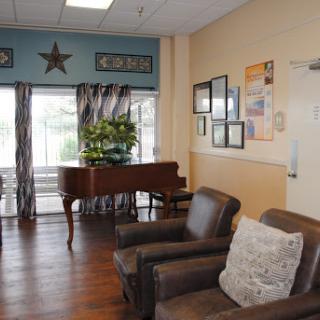 A cozy lounge area featuring comfortable seating and a piano, adorned with decorative elements and natural light.