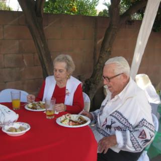 An elderly couple enjoys a meal together at an outdoor event.