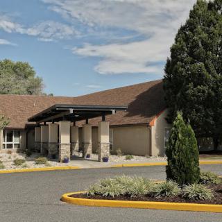 A building with a brown roof, surrounded by landscaped greenery and a clear sky in the background.