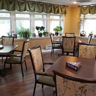 A cozy dining area with tables, chairs, and potted plants by the windows.