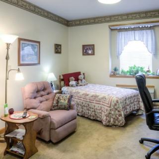 A cozy bedroom with a bed, armchair, and desk chair near a window.