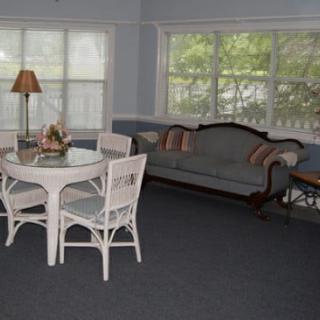 A cozy living room featuring a wicker dining set, a vintage-style sofa, and large windows allowing natural light to fill the space.
