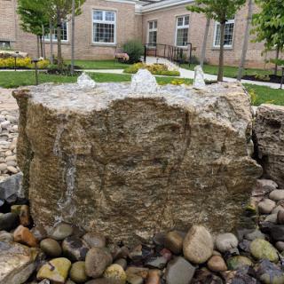 A tranquil water feature made of natural rock, surrounded by decorative pebbles in a landscaped garden.