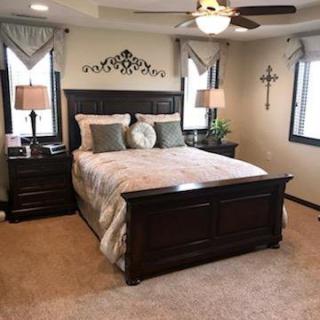 A cozy and elegantly decorated bedroom with a wooden bed frame, matching nightstands, and soft lighting from lamps and a ceiling fan.