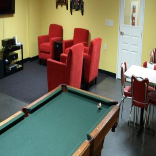 A cozy recreational room featuring a billiards table, red armchairs, and a small dining area.