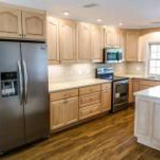 A modern kitchen featuring wood cabinets, a stainless steel fridge, and hardwood floors.