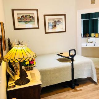 A cozy bedroom with a single bed, decorated with artwork and a classic lamp on a wooden bedside table.