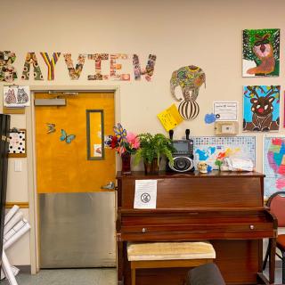 A classroom corner featuring a piano, artwork on the walls, and vibrant decorations.