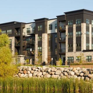 A modern apartment building with a stone facade overlooking a landscaped area.