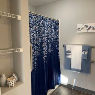 A tidy bathroom featuring a blue and white shower curtain, neatly arranged towels, and minimalist wall art.